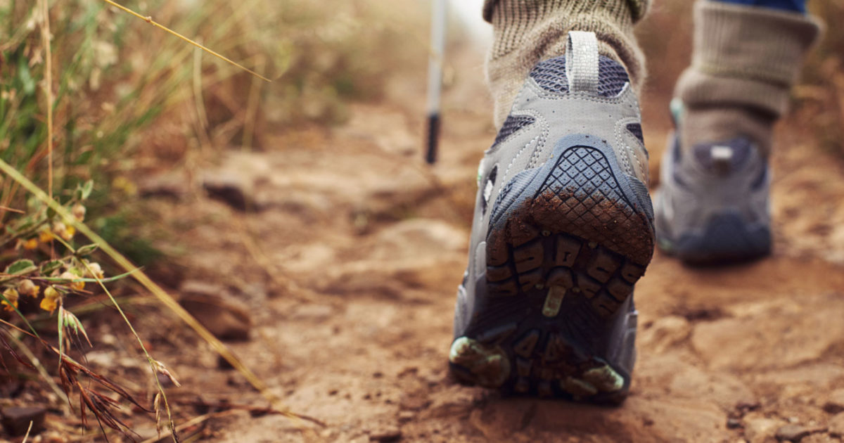 A close view of a person's foot, wearing a hiking boot, as they walk down a dirt trail.