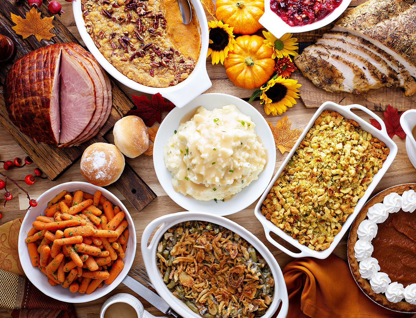 Assortment of Thanksgiving food including mashed potatoes, ham, carrots, green beans, and pie.