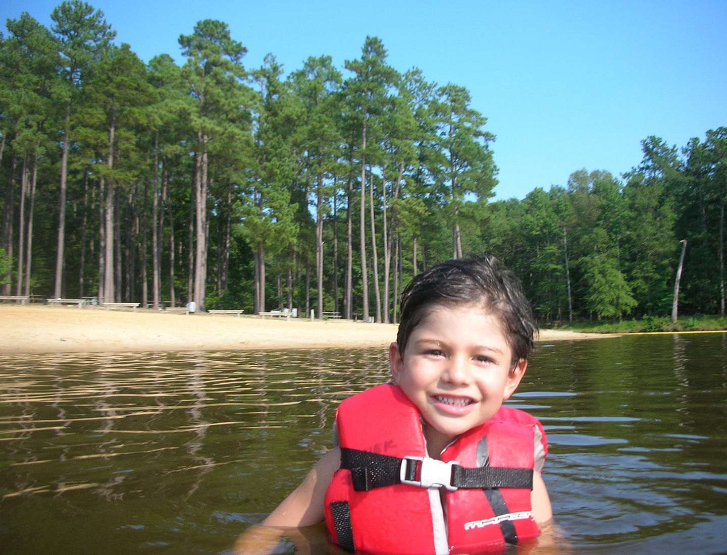 Former cardiology patient Lorenzo as young boy in a canoe, on a lake with large pine trees in the background.