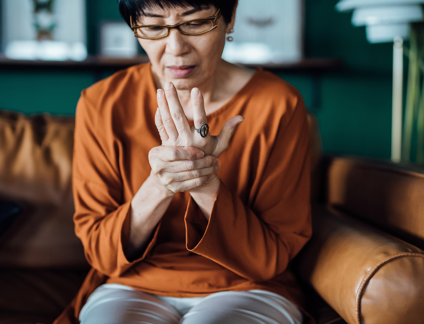An older woman holds her wrist in her other hand while sitting on the couch.