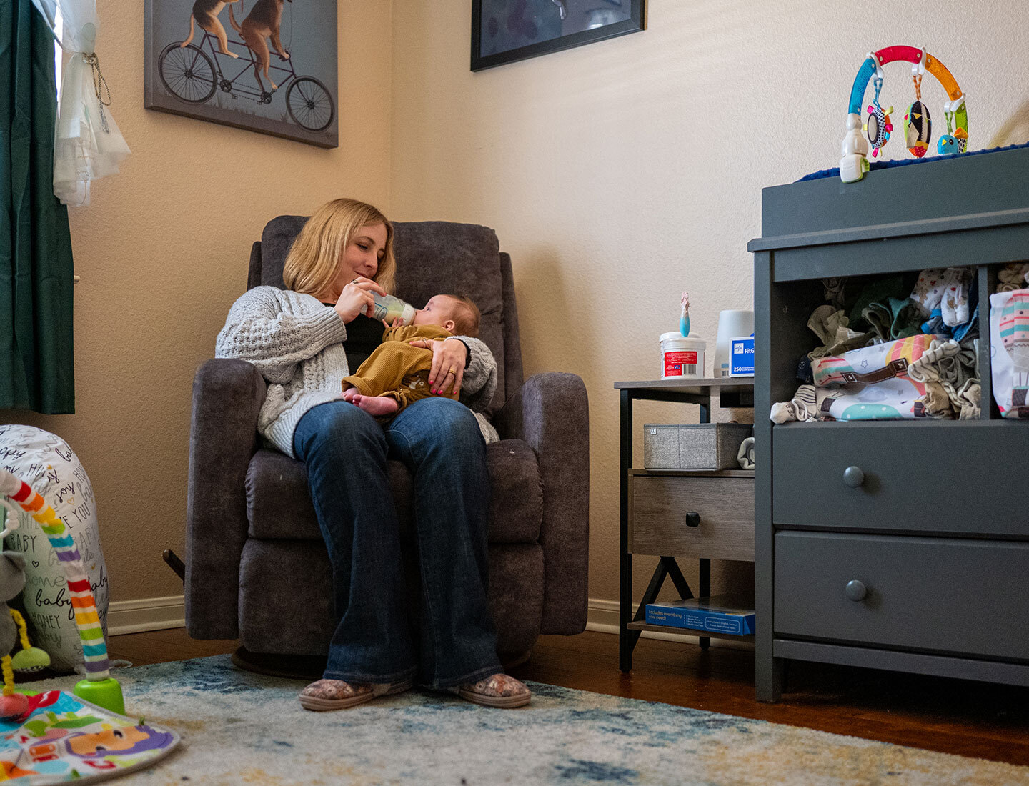 Woman in recliner feeds infant with a bottle in a cozy room, part of a UT Health Austin story about the world’s youngest patient receiving a Berlin Heart implant.