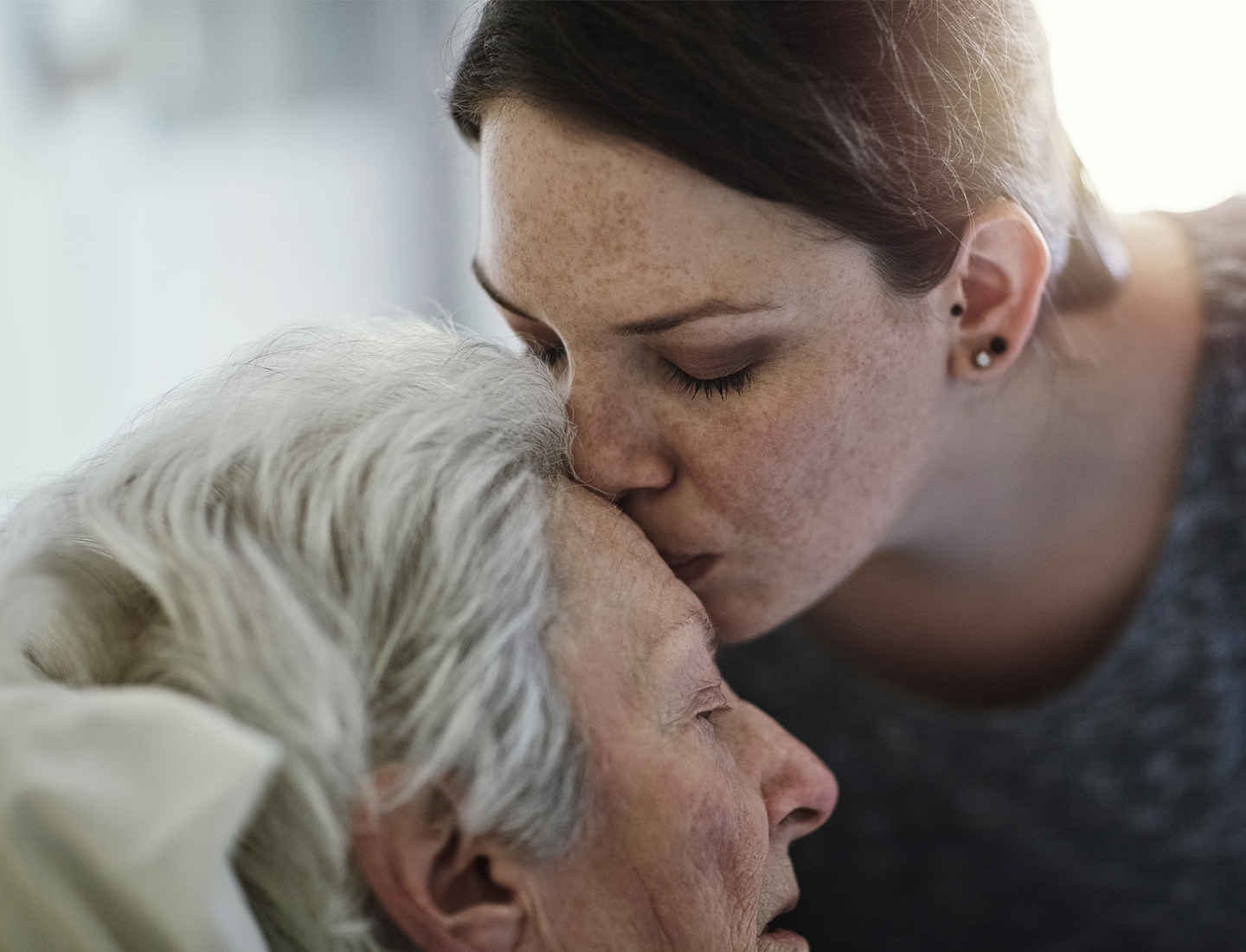 A woman kissing the forehead of her older loved one.