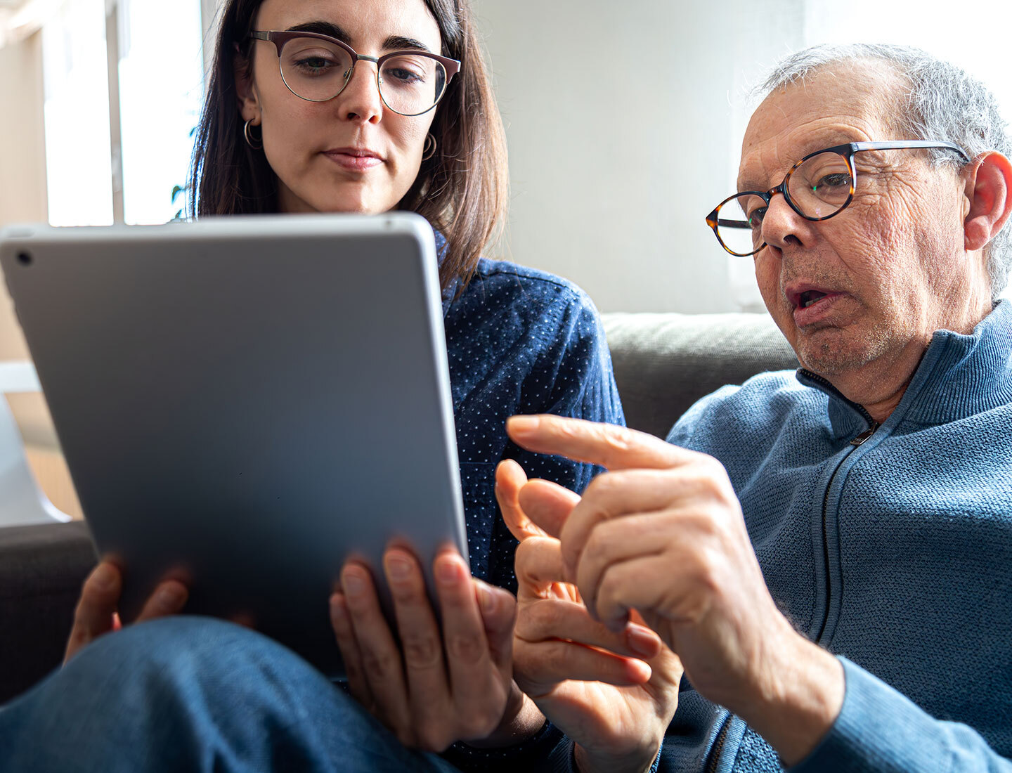 Older man and younger woman sit on a couch, looking at a tablet together to support cognitive health.