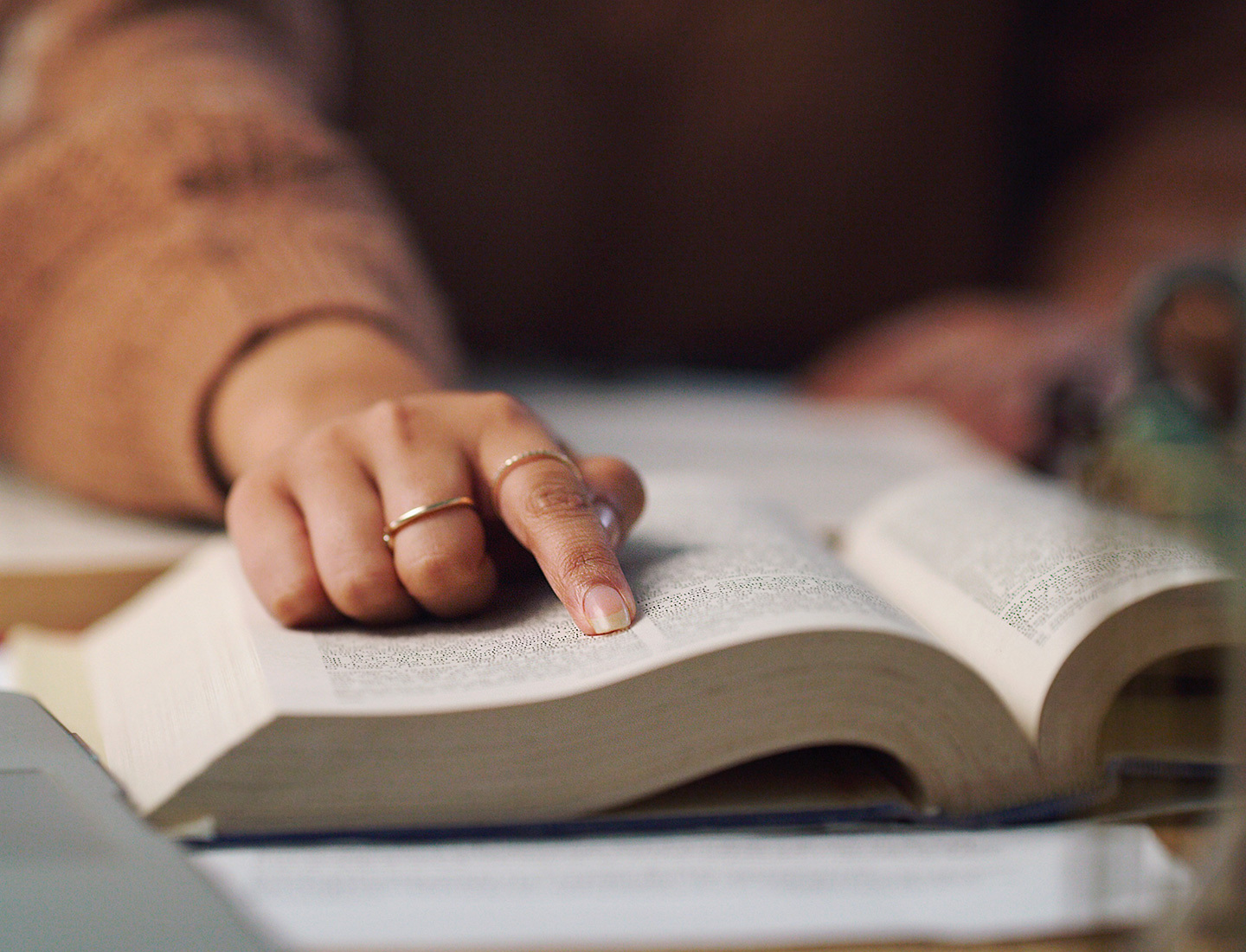 A hand with gold rings on two fingers pointing at text in a book.