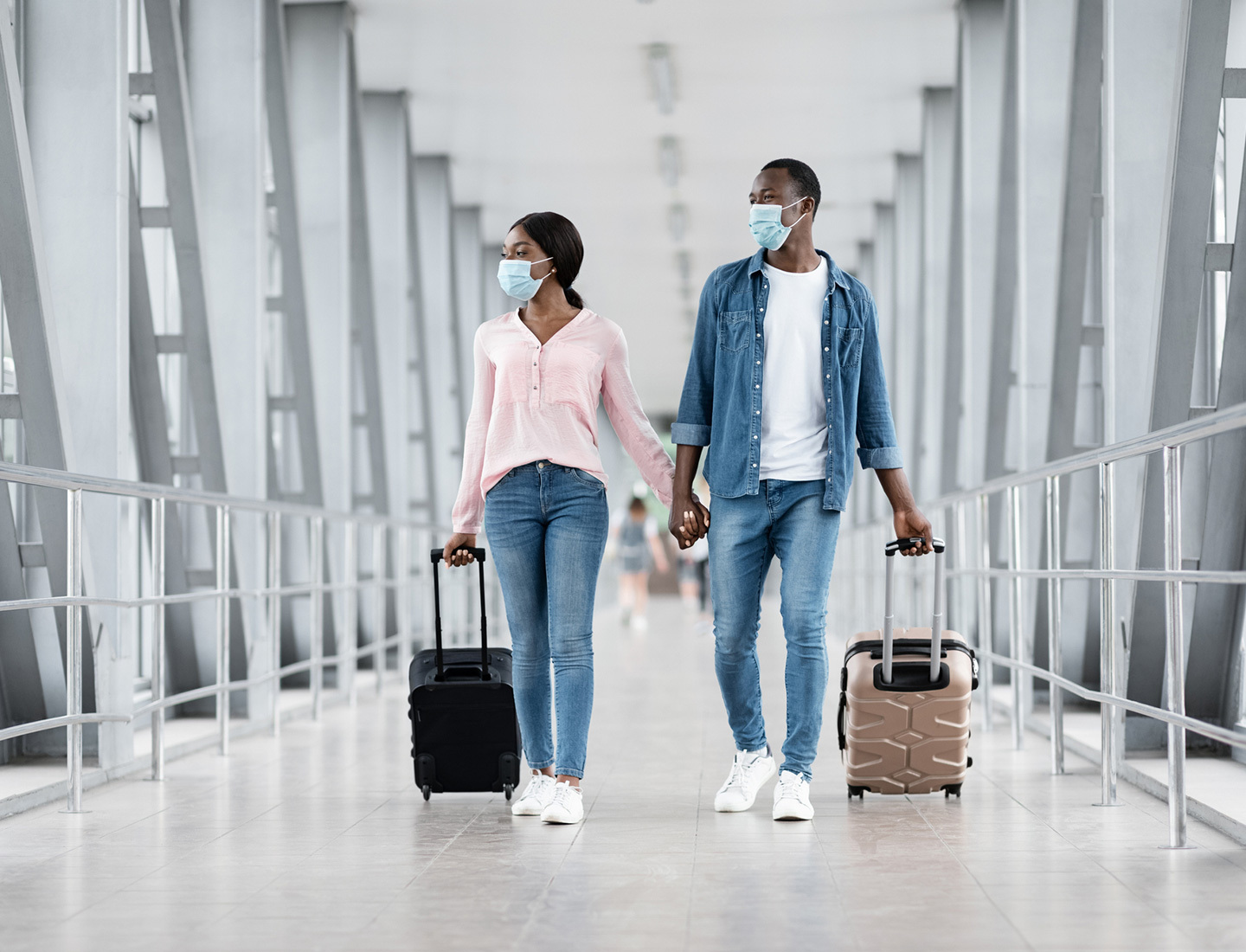 A couple wearing surgical masks tow their luggage through an airport.