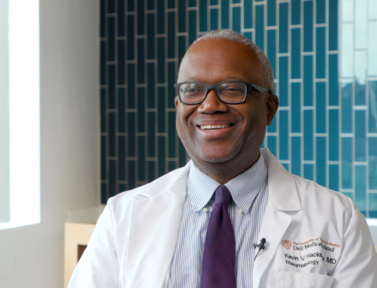 Dr. Kevin Hackshaw, rheumatologist, is featured during an interview, sitting in front of a teal tiled wall.