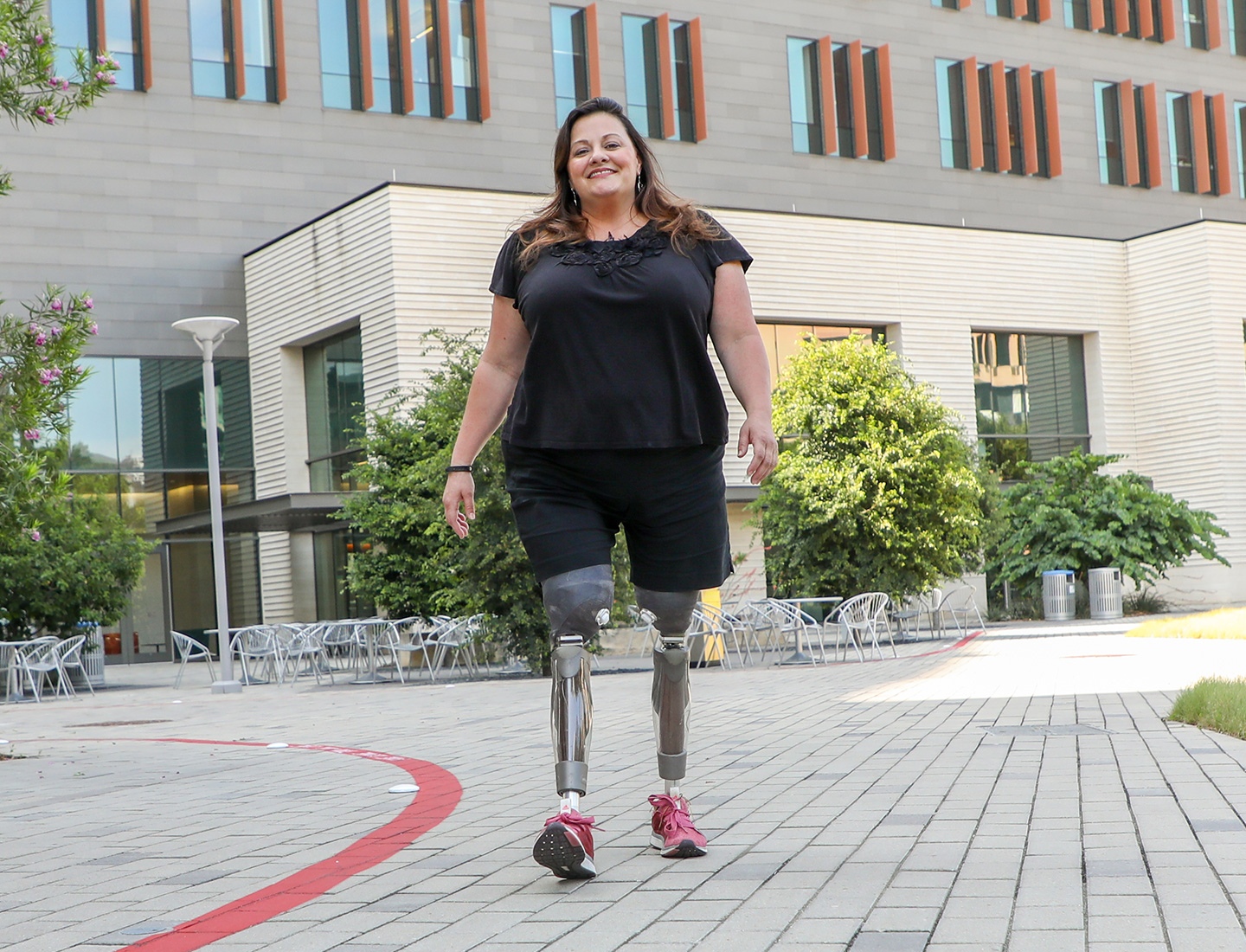 Heather, a patient with UT Health Austin's Musculoskeletal Institute, is seen walking with prosthetic legs across the courtyard at UT's Health Transformation Building.