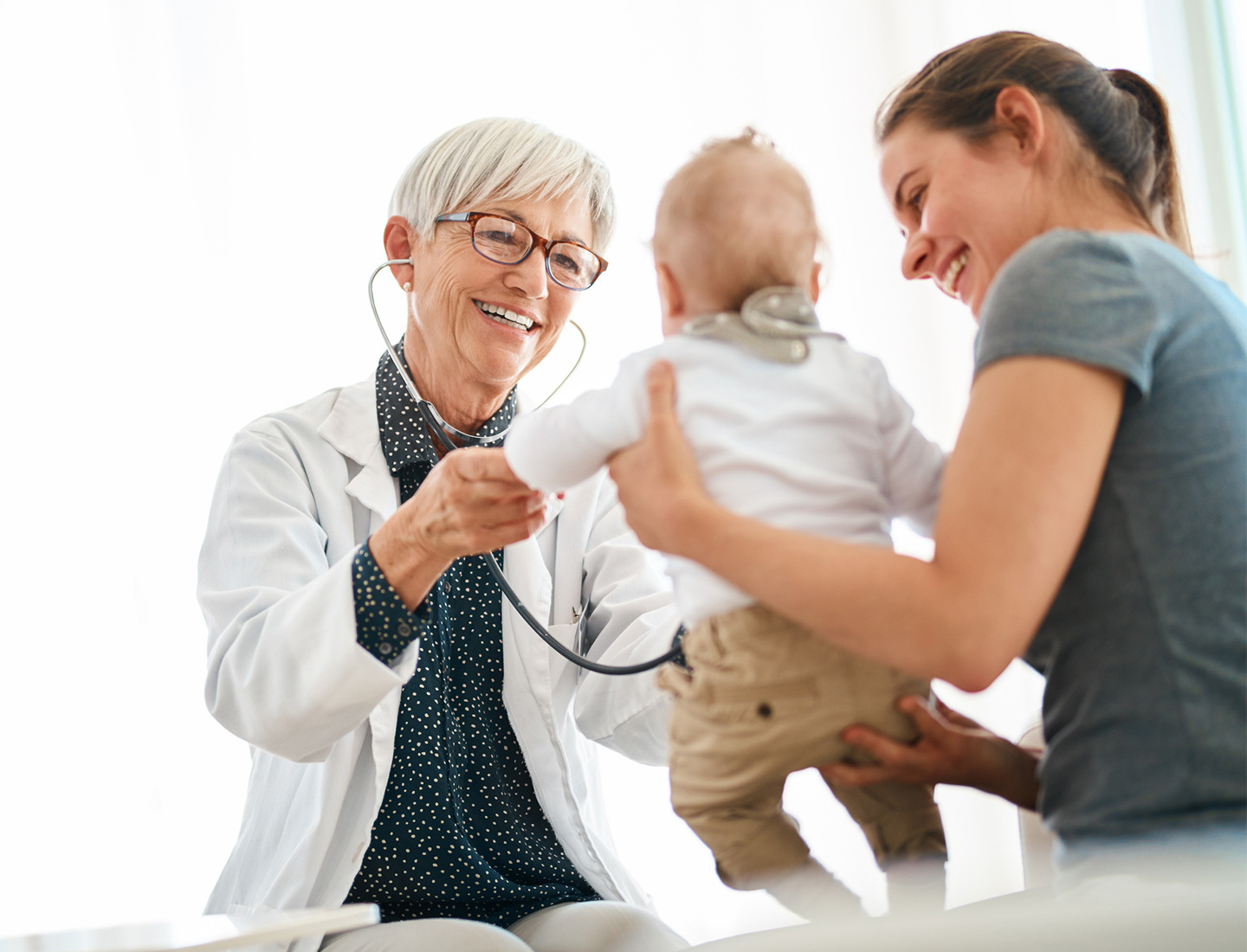 A mother holding her baby up to a smiling doctor holding a stethoscope. image