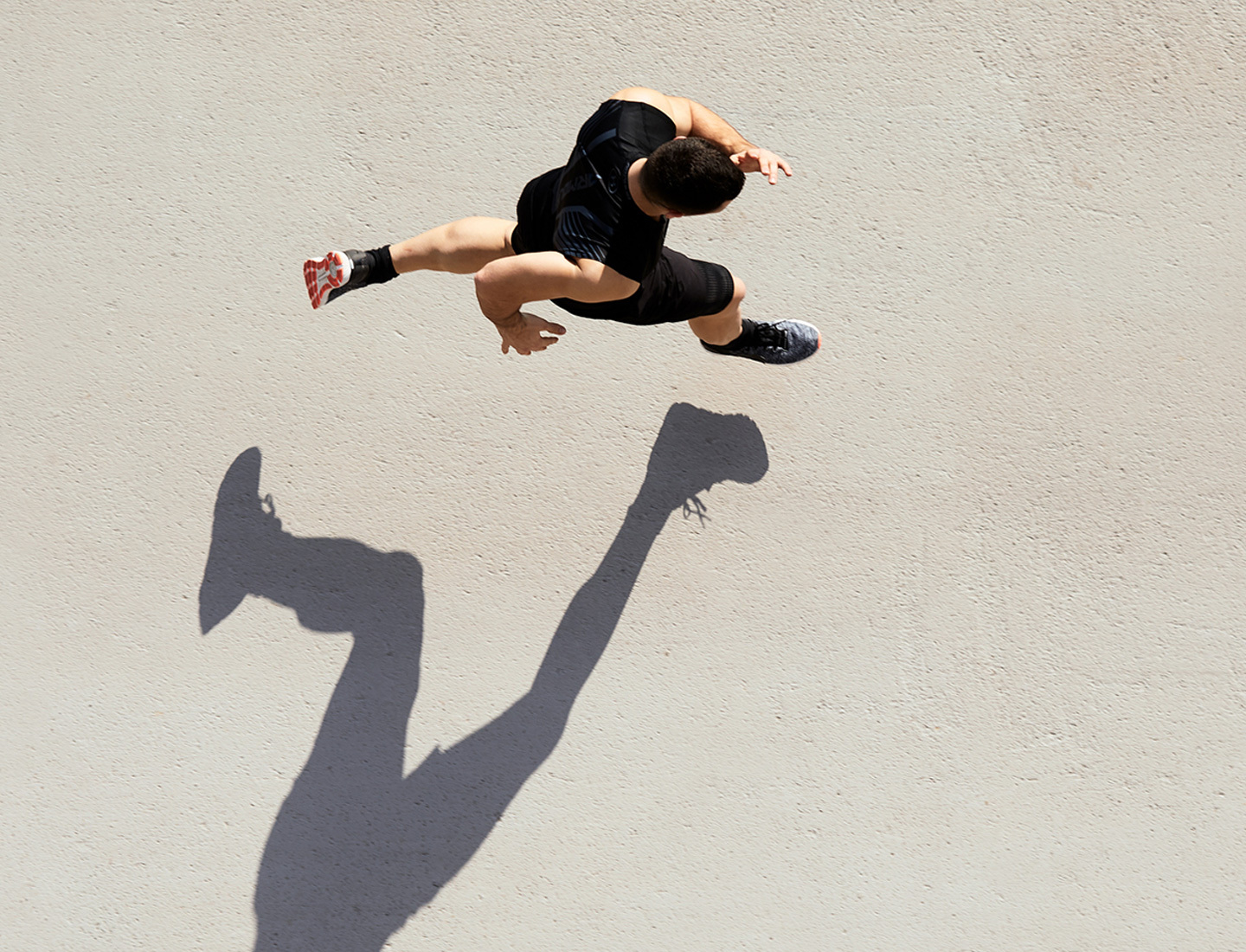 A man running as seen from above, casting a long shadow on the ground.