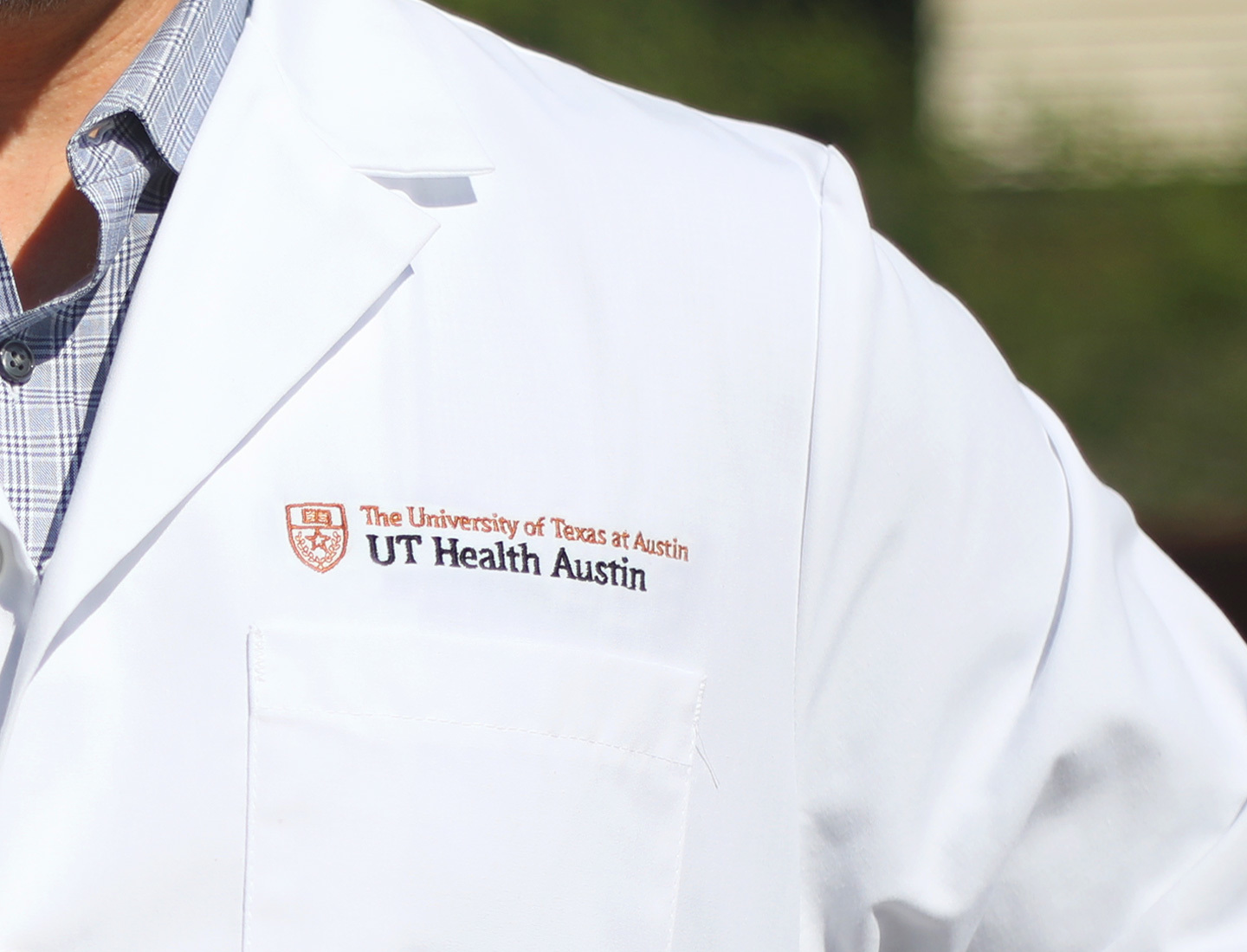 A close-up of a physician's coat left shoulder and chest showing the UT Health Austin logo.