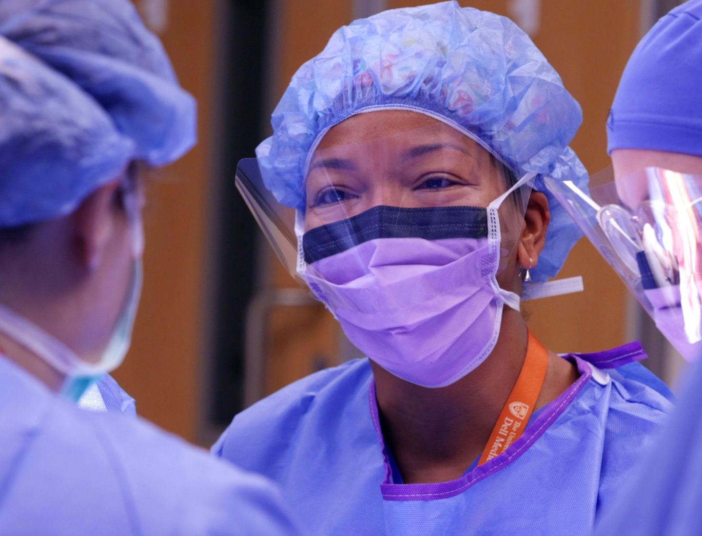 M. Yvette Williams-Brown, MD, wearing a surgical mask, face guard, scrubs, and head covering in the operating room surrounded by colleagues.