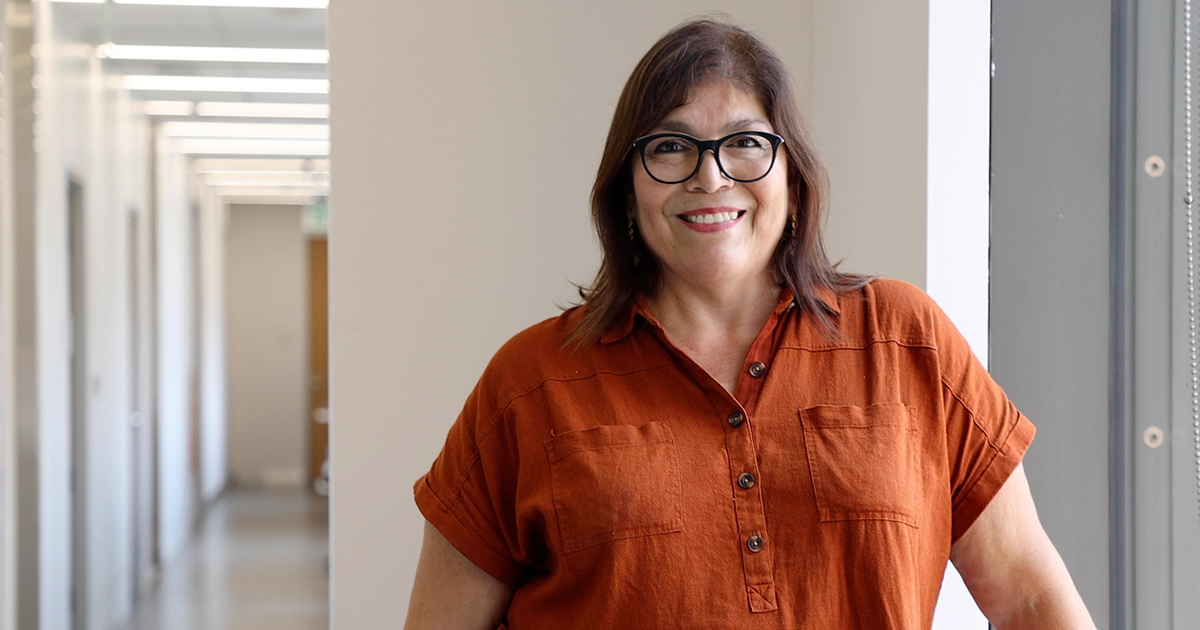 Sylvia Bhuiyan, a social worker on the UT Health Austin care team, smiles in a hallway wearing a burnt-orange top.