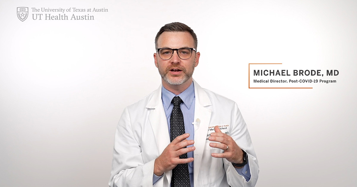 Michael Brode, MD, the Medical Director of the UT Health Austin Post-COVID-19 Program, wearing a white coat and speaking in front of a white backdrop.