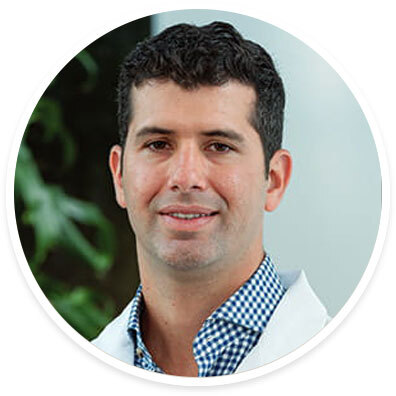 Headshot of Dr. Lucas Cardona smiling in a white coat over a blue checkered shirt.