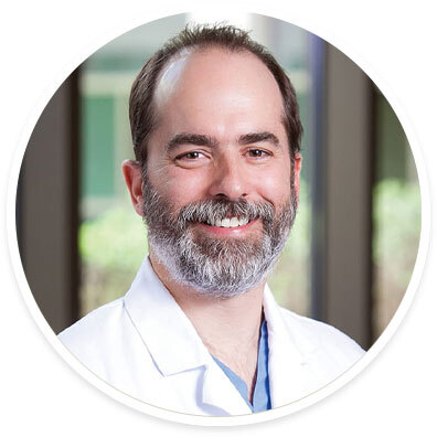 Headshot of Dr. Pedro Teixeira smiling in a white coat with a trimmed beard and short hair.
