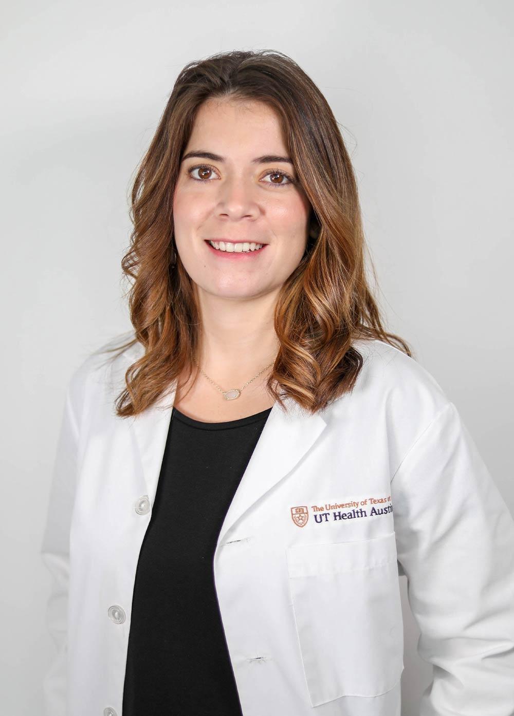 Joanna Lopez wearing a white coat and smiling in front of a white backdrop.