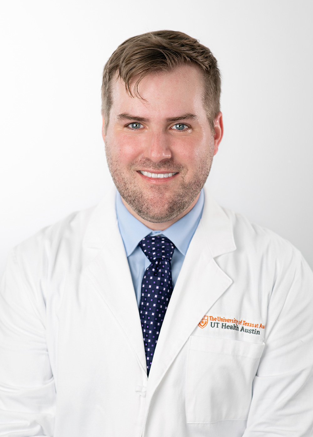 Pediatric cardiac critical care intensivist Austin Adair, MD, wearing a white coat and smiling in front of a white backdrop.